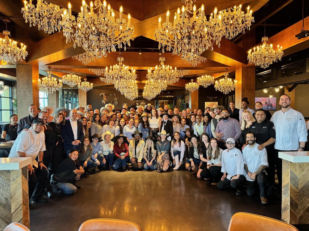 The full Haywire opening team, chefs in whites, servers and leadership, gathered under crystal chandeliers in a timber-beamed dining room